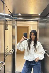 Blusa blanca con textura, cuello redondo con volados y mangas largas abullonadas.