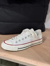 Zapatillas bajas de lona color blanco con cordones y puntera de goma. Detalle de doble línea roja y azul en la suela. Logo de la marca en la parte trasera de la base.