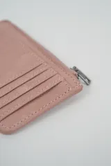 Billetera pequeña color gris claro con cierre de cremallera perimetral y tachas metálicas oscuras distribuidas en el frente.