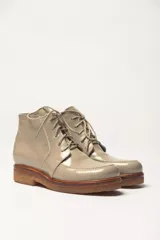 Bota corta de cuero vacuno con acabado charol negro, estilo botín de cordones. Presenta una suela de goma gruesa color caramelo con un borde visible.