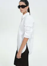 Camisa oversize blanca de popelina de algodón, con cuello camisero, cierre frontal oculto, mangas largas con puños abotonados y aberturas laterales.