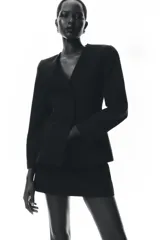 Blazer negra entallada, de escote pico y manga larga con hombreras. Tiene bolsillos delanteros de vivo y cierre frontal con botones a presión ocultos.