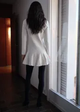 Vestido corto color crudo de tejido de punto fino con diseño de tablas en la falda, cuello redondo y manga larga.