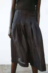 Pantalón culotte color marrón oscuro, de tiro alto con pliegues delanteros y tejido semitransparente efecto arrugado. Tiene forro interior y cierre lateral con cremallera oculta.