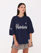 Camiseta deportiva azul marino de manga corta con cuello en V, logo de la NFL en el pecho y estampado frontal con el nombre del equipo New England Patriots. Diseño vintage con el logo del equipo en la manga y etiqueta conmemorativa en el ruedo.