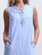 Vestido corto de algodón a rayas verticales celestes y blancas, con cuello a la base y abertura central acordonada. Incluye forro interno.