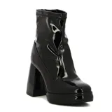 Bota corta de charol color crema, estilo botín, con caña elástica y puntera cuadrada. Presenta una plataforma delantera y un taco ancho y alto.