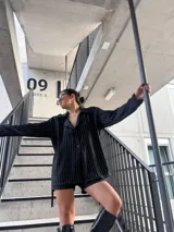 Blazer negro a rayas verticales blancas, con solapas de muesca, cierre cruzado con botones y corte entallado.