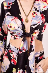 Camisa estampada con flores de colores sobre fondo negro, de corte cruzado, mangas 3/4 acampanadas y escote en V.