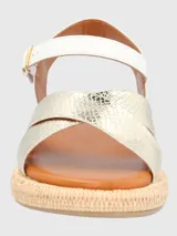 Sandalia con tiras cruzadas doradas con textura de piel de serpiente y ajuste con hebilla en el tobillo. Base tejida tipo esparto y plantilla acolchada.