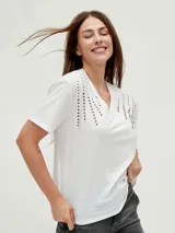 Remera negra de corte holgado con cuello en V y apliques de tachas doradas en los hombros.