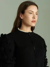 Cardigan marrón de tejido de punto con cierre frontal, cuello redondo y mangas abullonadas con apliques de pompones.