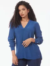 Blusa azul de corte amplio confeccionada en tejido de viscosa, con cuello en V, mangas largas con puños abotonados y aberturas laterales.
