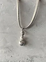 Collar con doble cadena, una tipo choker de cuero negro y otra más larga de cuero color beige, ambas con dije colgante de plata con forma de piedras irregulares.