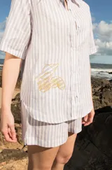 Camisa de lino a rayas verticales color naranja y blanco, de manga corta y corte oversize. Presenta bordados con motivos playeros en el frente y la espalda.