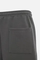 Pantalón jogger wide fit color gris oscuro, confeccionado en tejido de algodón compacto con elasticidad. Cuenta con cintura elástica ajustable con cordón, pliegues frontales, bolsillos delanteros y bolsillo trasero de parche.