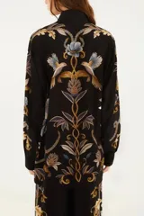 Camisa negra con estampado botánico y animal en tonos dorado y azul, de corte clásico y mangas largas.