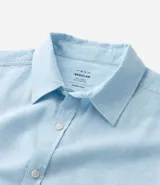 Camisa celeste de lino con cuello camisero, abotonadura frontal y mangas largas.