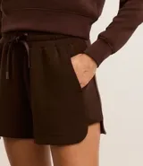 Bermuda deportiva femenina color marrón chocolate, modelo runner, con cintura elástica ajustable con lazo, bolsillos laterales y aberturas laterales.