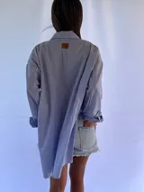 Camisa oversize a rayas verticales azules y blancas, con cuello clásico y cierre frontal con botones.