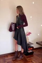 Falda asimétrica negra de cuero sintético, con diseño irregular, más corta en el lateral y con una caída más larga del otro.
