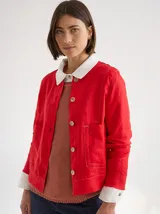 Chaqueta roja de lino y algodón, con cuello camisero blanco, cierre frontal con botones de madera, bolsillos de parche y corte recto.