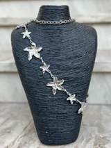 Cinto dorado de metal con eslabones y dijes en forma de estrella de mar. Incluye cadena regulable con dije esférico en el extremo.