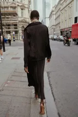 Camisa oversize color marrón oscuro confeccionada en tejido satinado con efecto arrugado, cuello solapa, manga larga con puños y cierre frontal con botones metálicos.