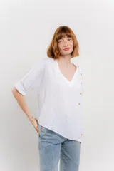 Blusa color naranja confeccionada en 100% lino, con escote en V, mangas cortas con vuelta y silueta amplia. Presenta terminación asimétrica y fila de botones decorativos en uno de los hombros.