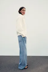 Camisa color crema de corte recto, confeccionada en algodón. Tiene cuello solapa, manga larga con puños abotonados, bolsillo de parche en el pecho y cierre frontal con botones.