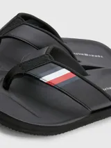 Ojotas negras Tommy Hilfiger con tira ancha de poliuretano acolchada y suela de goma EVA. Detalle de cinta distintiva con los colores de la marca en la tira.