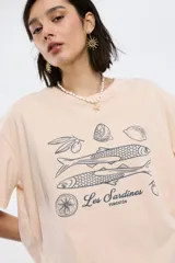 Remera color beige con estampado de sardinas, limones y aceitunas.