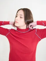 Polera negra de tela rib con cuello alto y mangas largas. Presenta pespuntes rojos en cuello, hombros y puños.