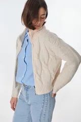 Cardigan color crudo de tejido de punto con diseño trenzado, cuello alto y cierre frontal con cremallera.