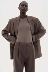 Pantalón sastrero marrón de corte holgado con tiro alto y cierre con corchete y botón ocultos. Piernas amplias con pinzas, pliegues adelante y atrás, bolsillos al bies y bolsillos decorativos atrás.