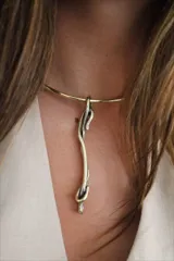 Gargantilla rígida dorada con dije colgante abstracto de bronce.