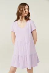 Vestido corto lila con cuello en V y mangas cortas. Tiene corte holgado y dos volados en la falda.
