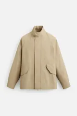 Parka color beige de corte relaxed fit, confeccionada en tejido técnico repelente al agua con costuras termoselladas, cuello alto, manga larga con puños ajustables con botón a presión, bolsillos de solapa en la cadera y cierre frontal con cremallera oculta por solapa con botones a presión.