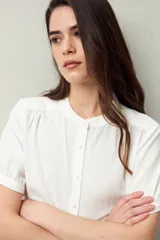 Camisa blanca de manga corta abullonada, cuello mao y botones forrados.