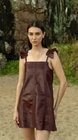 Vestido corto de cuero sintético color burdeos, con breteles finos regulables y volados en los hombros. Corte recto y largo a la altura del muslo.