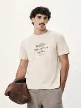 Camiseta blanca de algodón con cuello redondo y mangas cortas. Estampa rectangular con borde negro que contiene la frase "NATURAL ATMOSPHERE" en letras mayúsculas y una imagen de montañas y mar.