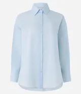 Camisa celeste de voile, corte oversized, con cuello clásico, cierre frontal con botones, mangas largas con puños largos y proceso de producción sostenible.