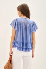 Camisa azul de algodón liviano con cuello redondo y gota en la espalda. Presenta detalle de bordado calado, terminación de volado en mangas y ruedo.