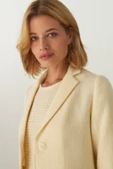 Chaqueta color crema de corte recto con cuello, solapa y bolsillos ojal. Forro solo en las mangas y terminaciones envivadas. Esquinas redondeadas y mangas con corte en puño que permiten transformarla en manga 3/4. Más larga en la espalda que en la delantera. Abrochadura con dos botones.