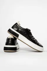 Zapatillas urbanas de cuero negro con cordones, suela blanca y detalles en marrón.