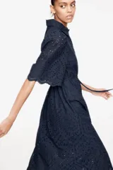 Vestido midi azul marino con broderie, cuello camisero, botones ocultos, mangas abullonadas al codo, cinturón fino con borlas y ribete festoneado en puños y bajo.