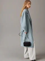 Cartera bandolera Calvin Klein negra con diseño acolchado de líneas verticales, correa de cadena plateada, cierre superior con cremallera y logo metálico frontal.