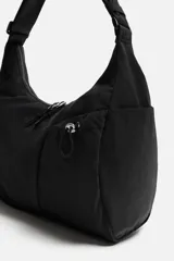 Bolso negro de tela técnica con correa de hombro ajustable. Tiene un compartimento principal con cierre de cremallera, un bolsillo interior con cremallera y tres bolsillos exteriores, uno de ellos con cremallera.