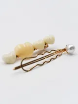 Set de dos broches para el pelo dorados, uno con forma de corazón color crema y otro con forma de horquilla con una perla blanca.
