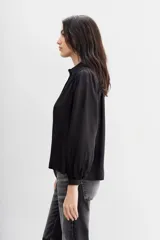 Camisa blanca de manga larga confeccionada en viscosa con acabado sandwash, de textura suave y aterciopelada. Cuello camisero con botón en forma de corazón y frunces en el canesú delantero y la espalda.